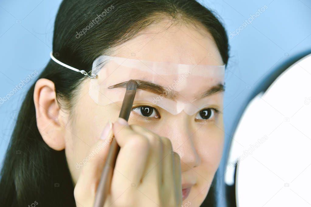 Asian woman applying cosmetics makeup, Eyebrows template head strap use for shaping and thickening perfect brows, Learning doing self makeup.