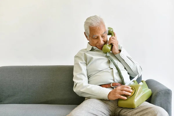 アジアの高齢者の老人が子供に電話をかけ、自宅でヴィンテージ電話で家族と話す孤独な祖父、高齢の高齢の親は家族に見捨てられた — ストック写真