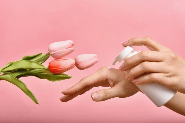 Hand applying natural lotion skincare, Cosmetic bottle containers packaging with tulip flower essence, Organic beauty product concept.