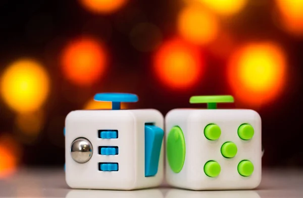 Fidget cube antis stress toy. Detail of finger play toy used for relax. Gadget placed on colorful bokeh background.