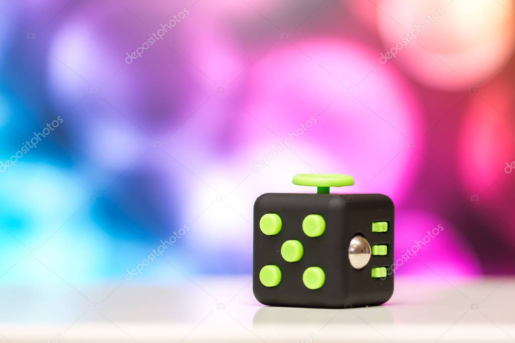 Fidget cube antis stress toy. Detail of finger play toy used for relax. Gadget placed on colorful bokeh background.
