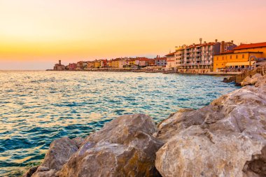 Güzel gün batımı Piran şehir, Slovenya üzerinde. Sihirli güneş Adriyatik Denizi ve Piran sahile ışığı. Yumuşak ışık gökyüzü ve mavi su ön planda. Taş duvara yakın Piran liman.