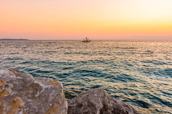 Gün batımı tekne Adriyatik Denizi üzerinde yukarıda. Sihirli yumuşak ışık ve mavi su Piran city, Slovenya yakınındaki. Taş rock ön planda.