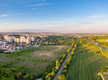 Gün batımında demiryolunun havadan görünümü. Arka planda şehir panoraması. Ağaçlar, çimenler ve çalılar ön planda