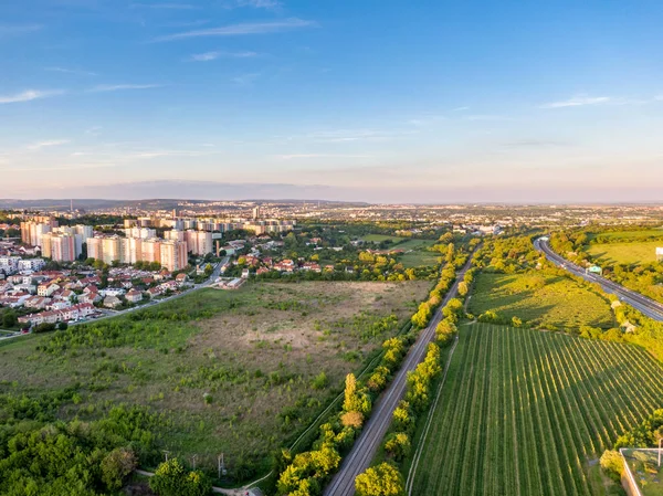 Luchtfoto van de spoorweg tijdens zonsondergang. Stadspanorama op de achtergrond. Bomen, gras en struiken op de voorgrond — Stockfoto