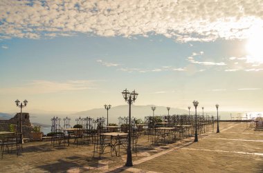 Akşam güneşinin kirişlerinde Yunan adası manzaralı bir açık hava kafe verandası. İyon Denizi sahili. Doğa ve seyahat. Arnavutluk, Vlora County, Saranda yakınlarında
