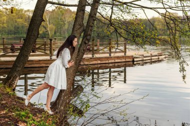 Beyaz elbiseli Genç bir kadın bir ağaca bir göl ve görünüyor üzerinde nehir suya sarıldı