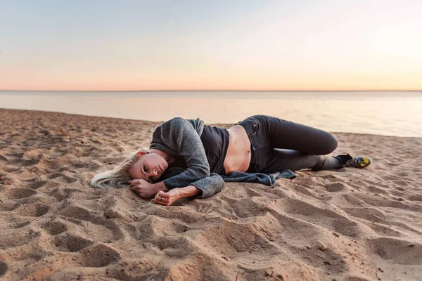 young sad abandoned woman lies on a sandy beach with a sunset on the background