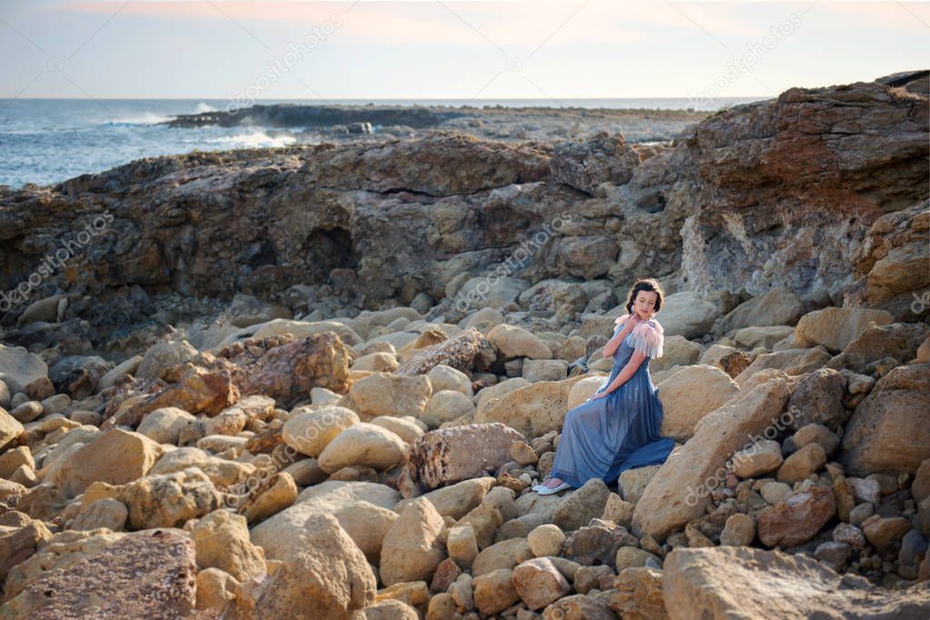 young cute girl sits in bliss on the rocks amidst the raging blue sea