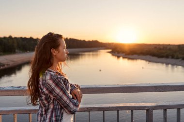 yaşam tarzı kıyafetler yakınındaki bir korkuluk güneş doğarken seyir köprüde duran kıvırcık saçlı Genç kız