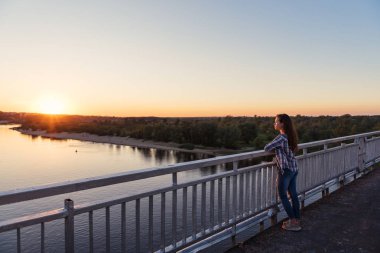 kız Genç ekose gömlek ve pantolon motu günbatımı manzaralı Nehri üzerinde duruyor