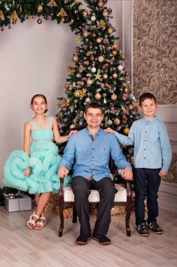 Baba ile kızı ve oğlu Noel arifesinde yılbaşı ağaç evde yakınındaki zarif giysiler