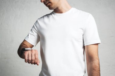 Boş beyaz tişört ve smartwatch, boş duvar, yatay stüdyo yakın çekim giyen genç adam