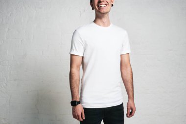 Genç gülümseyen adam beyaz boş t-shirt, yatay stüdyo portre, boş duvar