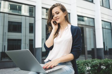 Genç kadın blogger kentsel Park açık havada modern laptop üzerinde çalışıyor. Kadın dizüstü bilgisayarda yazarak serbest ve smartphone tarafından müşteri ile konuşmak