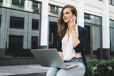 Kadın serbest iş bölgesinde sokakta laptop ile çalışma ve iş telefonla iş müşteri ile anlatılır.