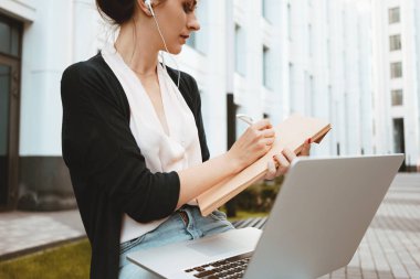 Genç kadın serbest meslek sahibi modern dizüstü bilgisayar, emek Pazar araştırması yapmak açık havada kentsel sokak üzerinde oturur. Mobil bilgisayardaki öğrenci iş kadın