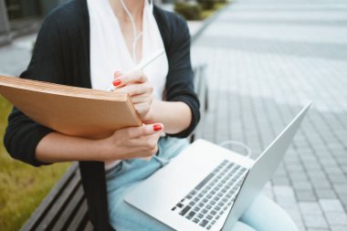 Kentsel alanda açık havada sınavlara hazırlanırken kız öğrenci üzerinde yakından görmek dizüstü bilgisayarı kullanıyor ve kağıt belgeleri. Kağıt üzerinde iş kadın yazar 