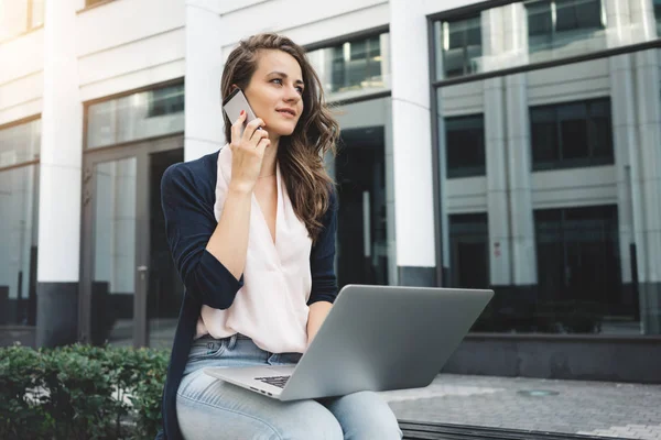 İş bölgesinde cadde üstünde laptop ile kadın serbest çalışma ve müşteriye telefonla konuşuyor