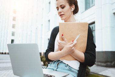 Kız öğrenci bir ders Üniversitesi önünde kentsel sokakta hazırlanıyor. Şehir Parkı içinde laptop ile çalışan genç iş kadını
