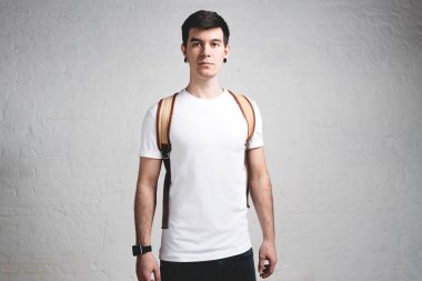 Boş beyaz t-shirt ve sırt çantası, boş çatı duvar genç gülümseyen adam portresi stüdyo