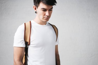Yakın çekim dalgın adam beyaz t-shirt ve sırt çantası takıyor görünümünü. Stüdyo portre