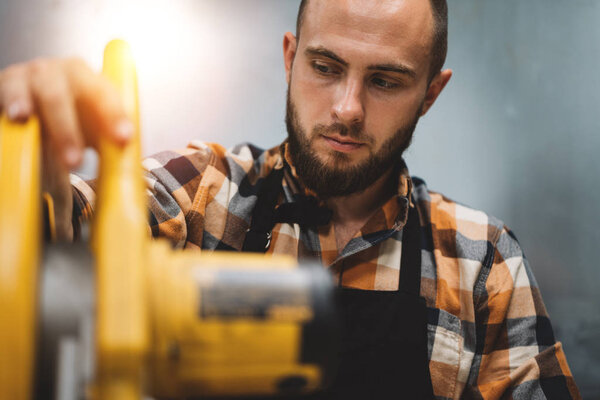 Bearded mechanic using electric grinding machine in service station. Servicing of machines