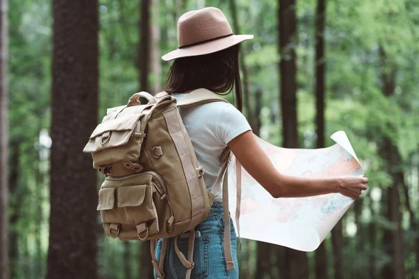Traveler hipster woman in forest with backpack searching direction on map