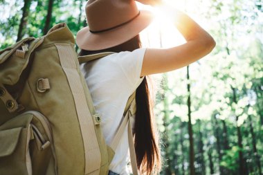 Arkadan Görünüş seyahat sırt çantası ve hippi kız şapka giyiyor. Yalnız ormandaki ağaçlar arasında açık havada üzerinde seyahat cesur kadın. Lens flare etkisi