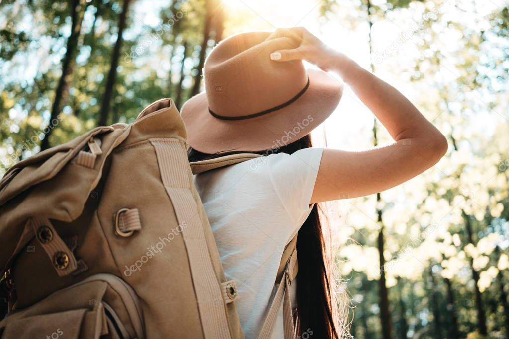 Back view of close-up traveler backpack and cute brave woman traveling alone among forest on outdoor