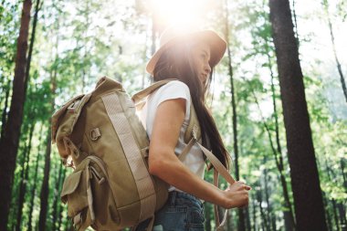 Sırt çantası ve yalnız ormandaki ağaçlar arasında üzerinde açık havada yolculuk şapka giyen cesur hipster kadın