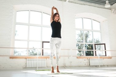 İnce kız bir güneşli sabah beyaz bir spor salonunda spor egzersizleri yapıyor. Sporcumuz önce egzersiz ısınma
