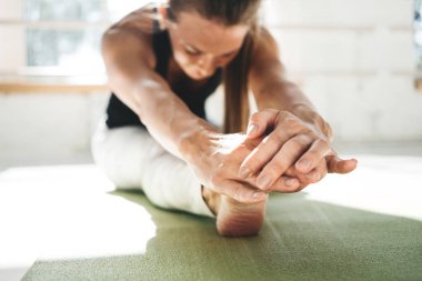 Kadın atlet güneşli spor salonunda sabah dinleme germe egzersizleri yapıyor. Fitness güçlü kadın ileri yoga mindere oturmuş onu bacak Germe bükme