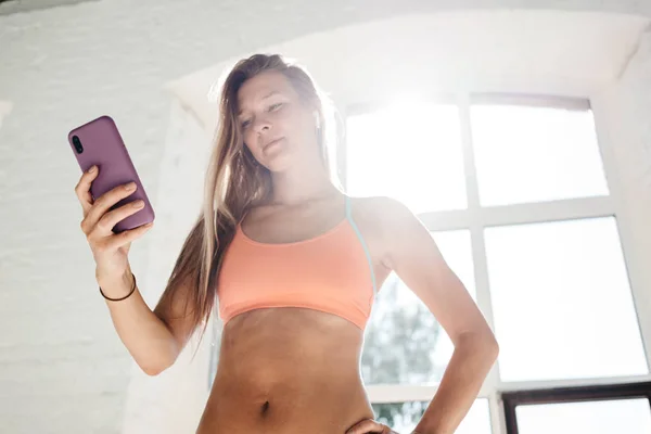 Ft woman counts calories and made post in blog after fitness workout. Healthy girl wearing sportwear hold smartphone in hand and considers calories in sport app aftrer training. Toned color