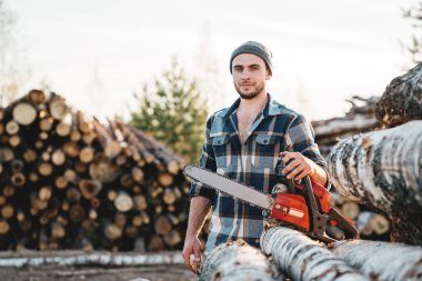 Ekose gömlek giymiş sakallı güçlü oduncu tutun el chainsaw çalışma için üzerinde kereste fabrikası