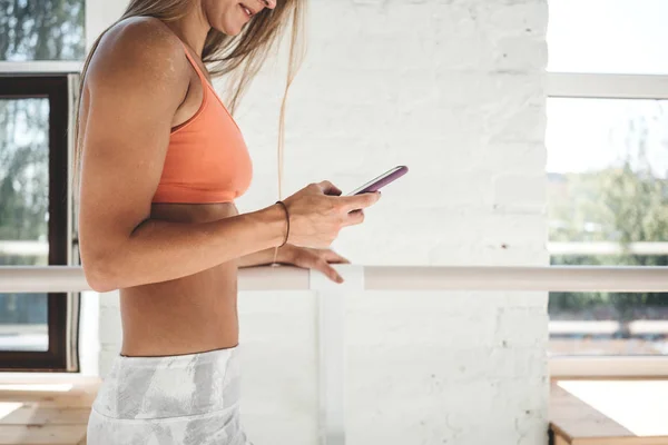 Happy fit woman counts calories and made post in blog after fitness workout. Healthy girl wearing sportwear hold smartphone in hand and considers calories in sport app aftrer training. Toned color