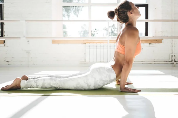 Yoga kapalı beyaz sınıf pratik uygun genç kadın portresi. Yakışıklı kız pratik kobra asana güneşli spor salonunda
