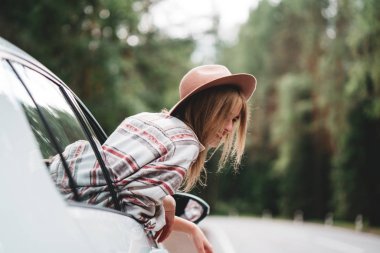 Araba penceresinden yolun manzarayı şapkalı güzel bir kadın. Taveler araba ile bir orman yolu rides