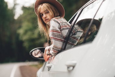 Güzel ve arabada oturan ve penceresinden vahşi yolda seyir kadın seyahat tarzı. Boho kız, yolculuk tutkusu. Kareli gömlek giymiş