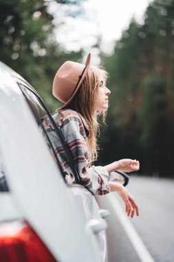 Happy hipster girl traveling adventure vacations. Boho woman sitting in car looking from window on beautiful view in country road clipart