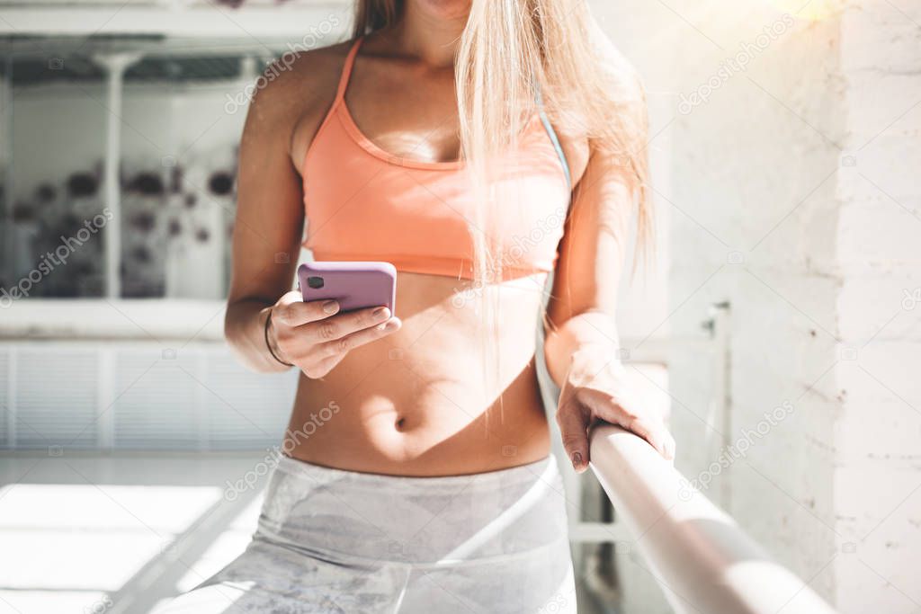 Happy fit woman counts calories and made post in blog after fitness workout. Healthy girl wearing sportwear hold smartphone in hand and considers calories in sport app aftrer training. Toned color