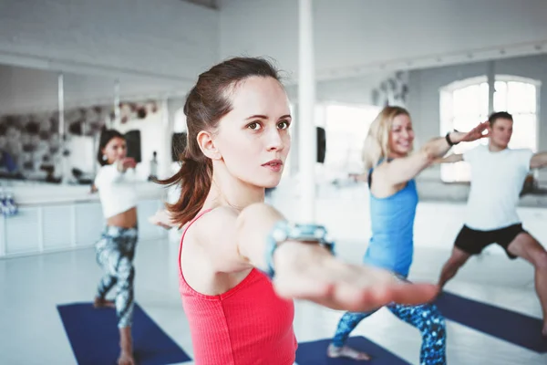 Close up portrait of young healthy woman doing yoga exercise indoor class together with group. Blurred background. Healthy and yoga practice