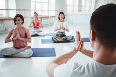 Adam koç trenler grubu Kadınlar yoga egzersizleri beyaz sınıfta sağlık korumak için. İnsanlar birlikte practis yoga teşkil etmektedir. Arka plan bulanık