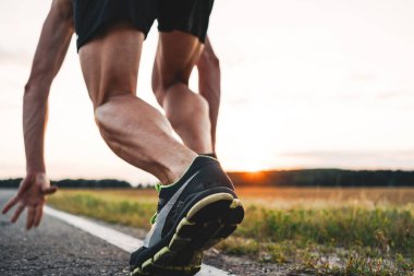 Güçlü ve kaslı sporcu atlet ayak açık asfalt yolda başlangıç poz görünümü kapatın. Arka plan bulanık