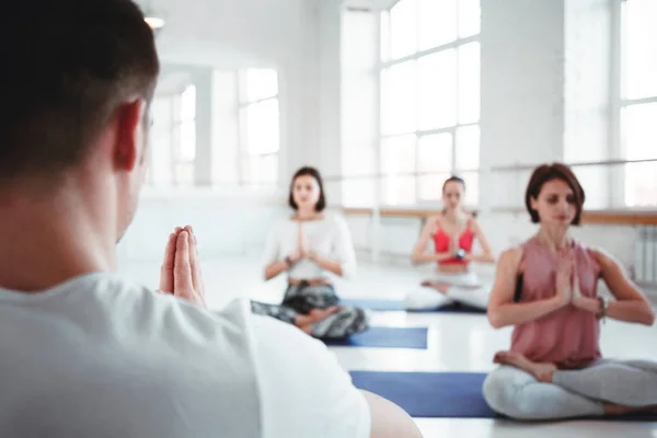 Man coach trains group of women yoga exercises for maintaining health care in white class. People together practis yoga poses. Blurred background