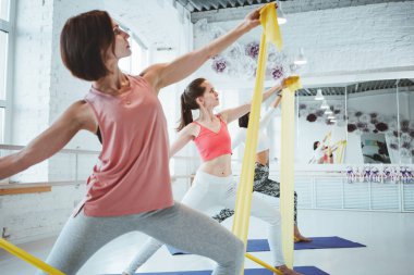 Grup Genç sağlıklı kadın yoga yaparken genişletici kasetle birlikte kapalı sınıf egzersiz. Sağlıklı yaşam konsepti
