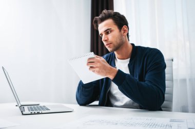Young businessman sits by table and make business plan using notepad and pen. Coworker man working in office space
