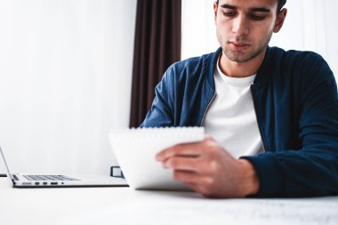 Concentrated businessman hold notepad while sitting by the desk at ofiice. Project manager using notebook 