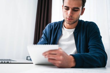 Young businessman sits by table and make business plan using notepad and pen. Coworker man working in office space