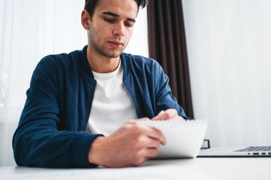 Dizüstü bilgisayar kullanarak ve modern evinin masada oturan proje planı hazırlanması sakallı adam. Ekran laptop arıyorum Not Defteri'nde yeni fikirler yazma adam konsantre